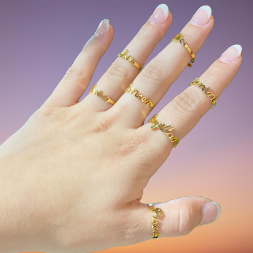Woman's hand displaying gold, scripted, zodiac name rings